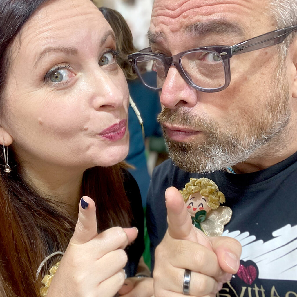 Due persone sorridenti indicano verso la fotocamera