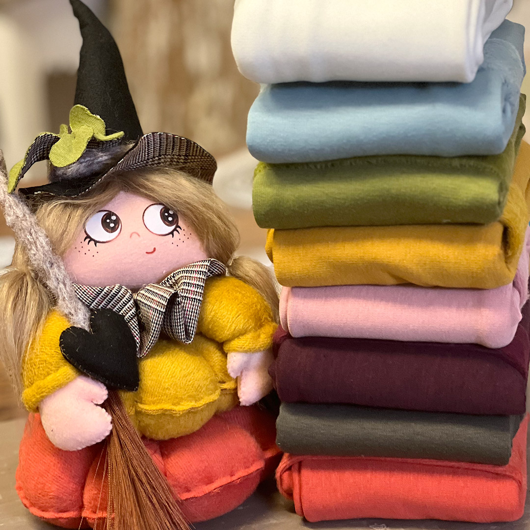 Bambola streghetta accanto a pile di tessuti colorati