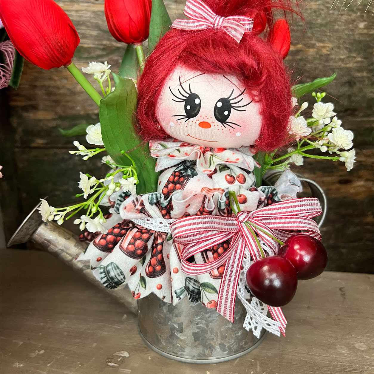Bambola rossa in annaffiatoio con fiori e ciliegie